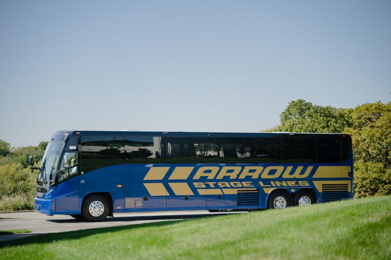 An Arrow Stage Lines motorcoach bus parked near a grassy lawn.