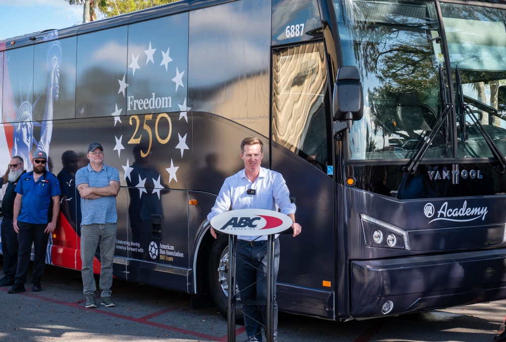 Fred Ferguson at a podium in front of a "Freedom 250" branded motorcoach addressing ABC employees